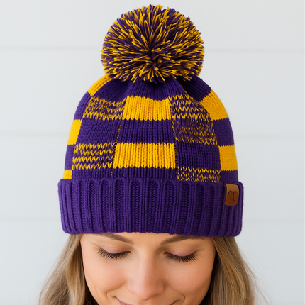 Purple and yellow striped knit beanie with pom-pom on a plain background